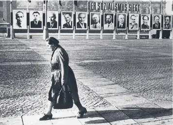  ??  ?? Before the wall came down: a woman walks along a deserted East Berlin street under the gaze of worldwide Communist leaders