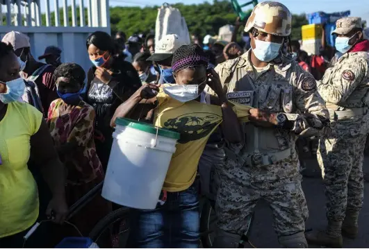  ?? Matias Delacroix, The Associated Press ?? A woman, who is denied entry into the Dominican Republic, tries to put on her protective face mask as a soldier removes her from a line for not initially wearing the mask at the border crossing in Dajabon, Dominican Republic, on Nov. 19.
