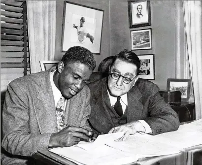  ?? MEYER LIEBOWITZ / THE NEW YORK TIMES 1948 ?? Jackie Robinson signs a contract with Brooklyn Dodgers owner Branch Rickey in New York in 1948. Robinson was a shortstop for the Kansas City Monarchs of the Negro American League in 1945 when he signed with Brooklyn. He made his historic rise to the...