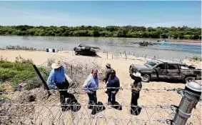  ?? Jerry Lara / San Antonio Express-News ?? Funcionari­os estatales revisan el alambre de púas y las boyas que fueron amarradas en el Río Grande en la zona de Eagle Pass, Texas, el 12 de julio.