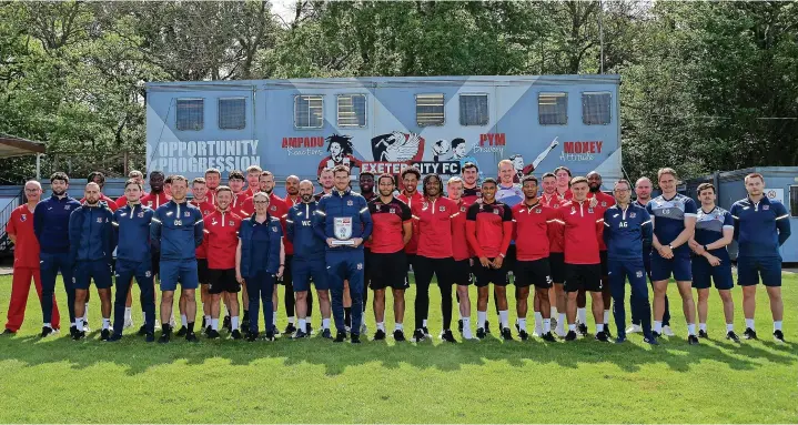  ?? Tom Sandberg/PPAUK ?? >
Exeter City’s promotion winning boss Matt Taylor poses with his trophy and the players and backroom staff at the Cliff Hill Training Ground