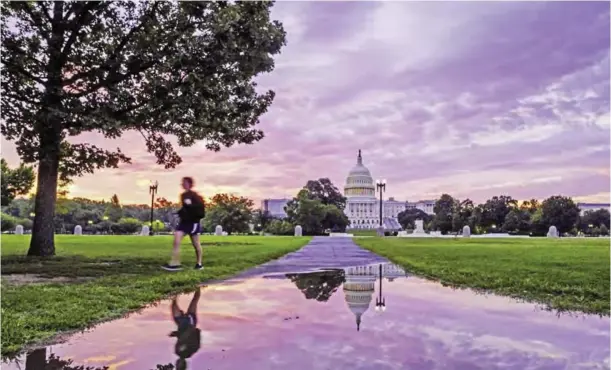  ?? — AP ?? A pedestrian walks past a reflection of the US Capitol in a rain puddle at daybreak in Washington yesterday.