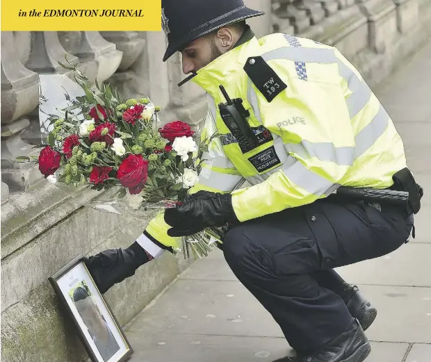  ?? DOMINIC LIPINSKI/PA VIA AP ?? A policeman places flowers and a photo of fellow officer Keith Palmer near the Houses of Parliament in London Thursday. Palmer died Wednesday after a knife-wielding man attacked him after driving a car into pedestrian­s within Parliament’s grounds in a...