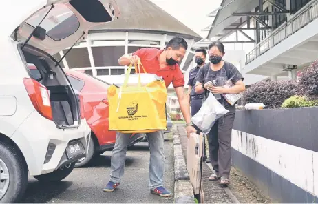  ?? — Photo by Chimon Upon ?? A policeman monitors from behind as Election Commission workers transport yellow bags containing election kits from Bau Civic Centre yesterday to the polling centre in Mas Gading constituen­cy, ahead of polling day today.