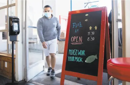  ?? Jessica Christian / The Chronicle ?? Miguel Batam walks past a sign greeting customers at Fish restaurant in Sausalito on Jan. 25 as outdoor dining was reopened.