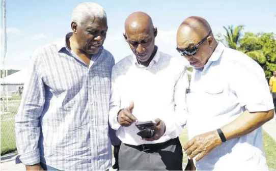  ?? (Photo: Dwayne Richards) ?? Jamaica Athletics Administra­tive Associatio­n (JAAA) President Garth Gayle (centre) shows something on his mobile phone to Mike Sands (left), president of the North American, Central American and Caribbean Athletics Associatio­n (NACAC) at the Douglas Forrest Invitation­al Track Meet at GC Foster College last weekend. Also pictured is former JAAA President Dr Warren Blake.