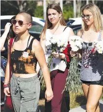  ??  ?? EMMA GONZALEZ (L), a senior at Marjory Stoneman Douglas High School, and others walk to campus on Feb. 25 in Parkland, Florida. Students and parents were allowed on campus for the first time since the shooting that killed 17 people on Feb. 14.