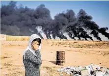  ?? Delil Souleiman / AFP via Getty Images ?? A woman covers her face as tires burn Wednesday on the outskirts of a town near the Syrian Kurdish town of Ras al-Ain.