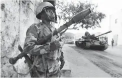  ??  ?? A Somali army soldier keeps guard as a tank rolls past after they captured the town of Barawe during the second phase of Operation Indian Ocean October 6, 2014.