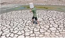  ?? ?? A man carries a plastic bucket across the cracked bed of a dried-up pond in Vietnam’s southern Ben Tre province.