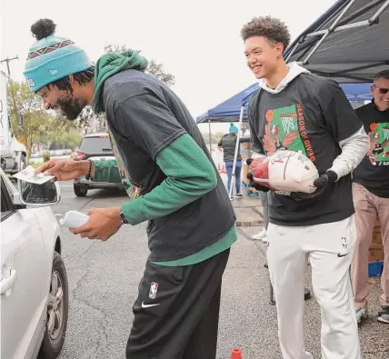  ?? Photos by Kin Man Hui/staff photograph­er ?? Spurs forwards Isaiah Roby, right, and Keita Bates-diop greet a family at a Thanksgivi­ng turkey giveaway Tuesday on the East Side that was a joint effort by the team, H-E-B and the San Antonio Food Bank to help families in need.