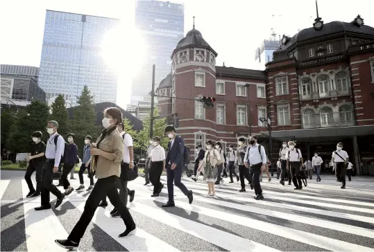  ?? The Yomiuri Shimbun ?? Commuters and others cross a pedestrian crossing in front of Tokyo Station on Monday, the first day after the state of emergency was extended.
