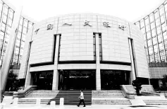  ??  ?? A staff member walks in front of the headquarte­rs of the PBOC, the central bank, in Beijing. China’s central bank will take on a beefed up role managing systemic risk in the country’s financial markets, state broadcaste­r China Central Television said,...