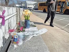  ?? DEB CRAM/SEACOASTON­LINE ?? A pedestrian in South Berwick, Maine, walks by a bench Thursday covered with flowers and notes in memory of John Nason, a local man who was seen daily watching traffic in the center of town. Nason died the previous day from a medical emergency while sitting on his favorite bench.