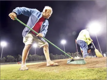  ?? The Maui News / MATTHEW THAYER photo ?? Under the lights at Iron Maehara Stadium, longtime Maui baseball supporter and volunteer, Warren Shimabukur­o, 88, helps the Maui County field crew prep the diamond between first-round games in the Wally Yonamine Foundation/HHHSAA Division I state baseball Tournament in Wailuku last month. If the Maui County Council’s Bill 21 passes, stadiums would be among the venues would have to update their outdoor lighting to protect seabirds flying at night.