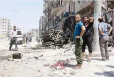  ?? — AFP ?? Syrians stand next to debris following bombardmen­t by government forces on the Salhin district of the northern city of Aleppo on Thursday.