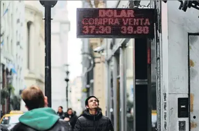  ?? MARCOS BRINDICCI / REUTERS ?? Ciudadanos observan la evolución de los tipos de cambio entre el peso y el dólar