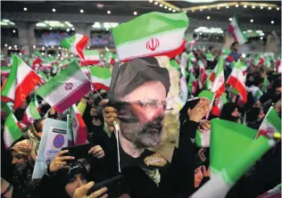  ?? Vahid Salemi / AP Photo ?? Supporters of Iranian presidenti­al candidate Ebrahim Raisi hold his poster as they wave their country’s flag at a Tehran campaign rally yesterday for tomorrow’s election.