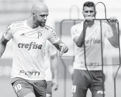  ?? Cesar Greco/Palmeiras/Divulgação ?? O volante Felipe Melo participa de um treinament­o do Palmeiras na Academia de Futebol, observado por Thiago Santos (ao fundo); o Pit Bull cumpriu gancho no Choque-Rei e vai voltar contra o Jorge Wilsterman­n