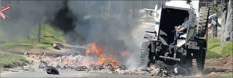  ?? Picture: EUGENE COETZEE ?? FIRED UP : Members of the Public Order Policing unit drive through a burning barricade in Victoria Drive yesterday