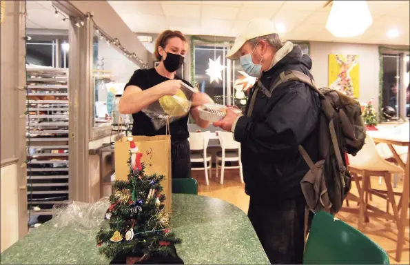  ?? Christian Abraham / Hearst Connecticu­t Media ?? Mothership Bakery & Cafe owner Anna Llanos helps a guest with a take-out dinner during a pre-Christmas dinner for Danbury- area homeless, day laborers and anyone in need Wednesday. Volunteers from the Jericho Partnershi­p food pantry helped bring in the guests for the dinner and staff at Mothership prepared and served the meals.