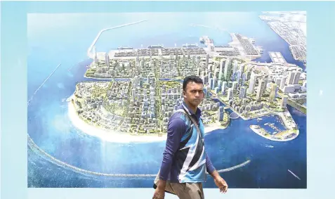  ?? — AFP photo ?? A man walks past a billboard showing the intended design of the Chinese-funded Port City on reclaimed land in Colombo.