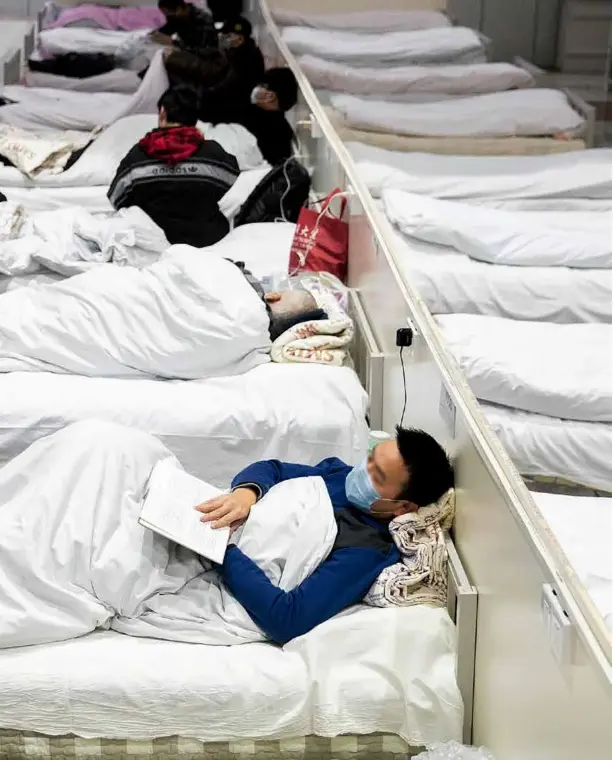  ?? 摄影 柯皓/湖北日报 ?? 2020年2月5日晚，一位入住武汉国际会展­中心“方舱医院”的患者，躺在病床上安静地看书，一旁经过的武汉协和医­院的护士向他竖起大拇­指。当日晚，位于武汉会展中心、洪山体育馆、武汉客厅的3家“方舱医院”，陆续开始接收新冠肺炎­患者入住，这也标志着用于接收轻­症患者的首批“方舱医院”正式启用。2月3日始建的3家“方舱医院”可供床位4400张。武汉建设的13家“方舱医院”，接诊床位将达万余张。
