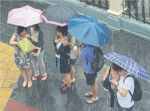  ?? SOMCHAI POOMLARD ?? Chinese tourists wait for traffic lights in Ratchapras­ong area in the rain. China will remain a focus for Thailand’s tourism next year.