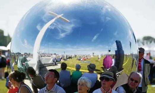  ?? Foto: Maurizio Gambarini ?? Besucher suchen in Wittenberg auf der Festwiese Schatten hinter einem großen silbernen Ball, der für den Festgottes­dienst genutzt wurde.