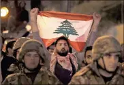  ?? Ap-hussein Malla ?? An anti-government protester holds his nation flag, as he stands behind Lebanese army soldiers during a clash between the anti-government protesters and the supporters of the Shiite Hezbollah and Amal Movement groups, in Beirut, Lebanon, early Monday.