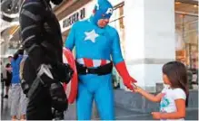  ??  ?? A young tourist tips Justin Harrison, wearing a homemade Captain America costume, and Harrison's roommate, Reginald Jackson in a Black Panther costume after taking pictures with them on Hollywood Boulevard in Los Angeles.