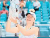  ?? MICHAEL REAVES/GETTY ?? Iga Swiatek raises the Butch Buchholz Trophy after defeating Naomi Osaka in the singles final Saturday in Miami Gardens, Florida.