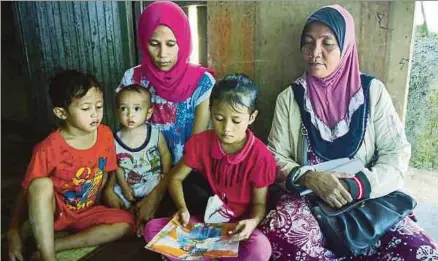  ?? [ FOTO POLIANA RONNIE SIDOM / BH ?? Nadin Junianti, melihat gambar suaminya bersama tiga anak dan ibu mentuanya, Zuana Laudiato, ketika ditemui di rumah mereka di penempatan setinggan berhampira­n Sim-sim, di Sandakan.