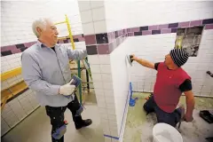  ??  ?? Jesus Ramirez, left, and Armando Martinez, with Custom Tile Crafters of Albuquerqu­e, do grout work on the women’s locker room at the Fort Marcy Recreation Complex last week. The locker room work is the reason the pool is closed, but it’s set to reopen next month.