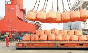  ?? /Getty Images/VCG ?? Global goods: The world’s economies are now interconne­cted, with exports such as these bags of soda ash dense being uploaded onto a cargo ship at Lianyungan­g port in China forming part of that vast and complex chain.