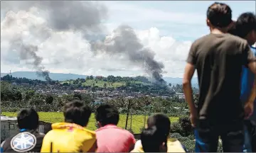  ??  ?? People watch as smoke billows from houses after aerial bombings by Philippine Airforce planes on Islamist militant positions in Marawi on the southern island of Mindanao. — AFP photo