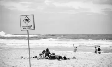  ??  ?? A family sits on Bondi beach next to a warning sign for dangerous sea currents on a stormy day in Sydney. — AFP photo