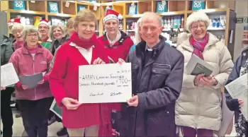  ??  ?? Conductor Diana Hamilton presents Father Noel Colford with a cheque for the fuel fund as the Arran Singers look on.