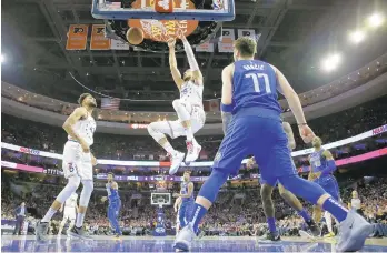  ?? MATT SLOCUM / AP ?? Ben Simmons hangs on the rim as Jonah Bolden and Dallas' Luka Doncic look on.