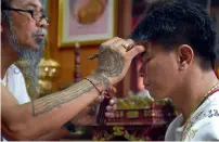  ?? AFP ?? ‘Hermit’ Toon inscribing a protective charm with holy oil on the forehead of a Taiwanese client during a ritual in the northern Thai province of Khon Kaen. —