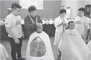  ??  ?? HUANG mengguntin­g rambut salah seorang peserta pada program ‘Go Bald 9 Satellite Shave’ di Sarikei.