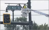  ??  ?? A constructi­on worker works to install a new12Mile Road sign on a decorative traffic signal pole at 12Mile and Utica Road in Roseville.
