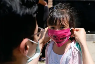  ?? ASSOCIATED PRESS ?? In this June 10, 2020, file photo, Olivia Chan’s father helps her with a new mask she received during a graduation ceremony for her Pre-k class in front of Bradford School in Jersey City, N.J. School districts across America are in the midst of wrenching decisions during the summer about how to resume classes in settings radically altered by the coronaviru­s pandemic, with socially distanced school buses, virtual learning, outdoor classrooms and quarantine protocols for infected children as the new norm.