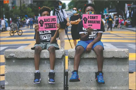  ??  ?? Tyshawn, 9, (left) and his brother Tyler, 11, of Baltimore, hold signs saying “Black Lives Matter” and “I Can’t Breathe” as they sit on a concrete barrier June 24 near a police line as demonstrat­ors protest along a section of 16th Street been renamed Black Lives Matter Plaza in Washington. (AP/Jacquelyn Martin)