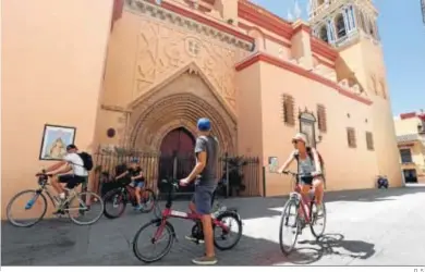  ?? D. S. ?? Cuatro turistas en bicicleta junto a una de las entradas a la parroquía de Santa Ana, en Triana.