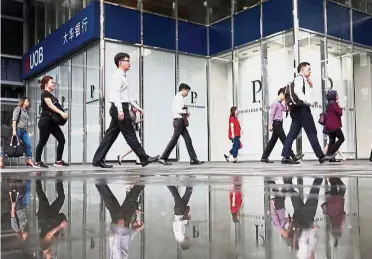  ?? — Reuters ?? Aging workforce: Office workers pass a UOB bank branch in Singapore’s central business district. The city state will face a double whammy: a shrinking workforce and slower progress than Asian neighbors in getting more people into the labour market.