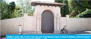  ?? — AFP ?? PALMA: A cyclist rides in front of the main gate of the Marivent Palace in Palma de Mallorca, where the Spanish Royal family will spend their summer holidays.