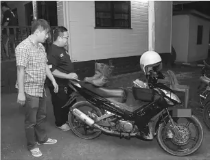  ??  ?? Ong (left) shows the motorcycle used by the suspect in the break-in.