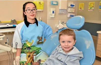  ??  ?? Oral health therapist Michelle Looc wears a gown featuring the Tree Hutt characters that will help put youngsters like Nico Beddis, 5, more at ease during their check-ups.