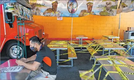  ?? .Jae C. Hong The Associated Press ?? Abel Gomez waits at a Los Angeles food truck July 1 as dining tables are sealed off due to the coronaviru­s pandemic. California Gov. Gavin Newsom has extended the closure of bars and indoor dining and ordered gyms, churches and salons closed as new cases surge.